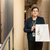 Rita Macheda displays a plant specimen for the camera. There are metal cabinets in the background.