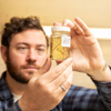 A herbarium staff member holds a labelled jar filled with ethanol and a few pieces of plant material to the light.